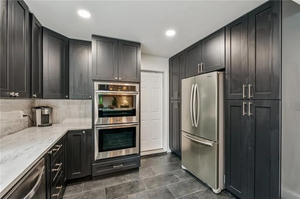 Kitchen featuring dark cabinetry, appliances with stainless steel finishes, light stone counters, decorative backsplash, and recessed lighting
