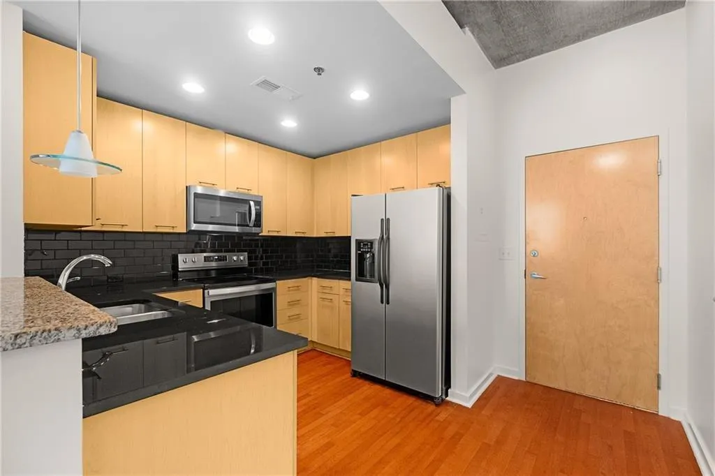 Kitchen featuring light brown cabinetry, light wood finished floors, stainless steel appliances, and a sink