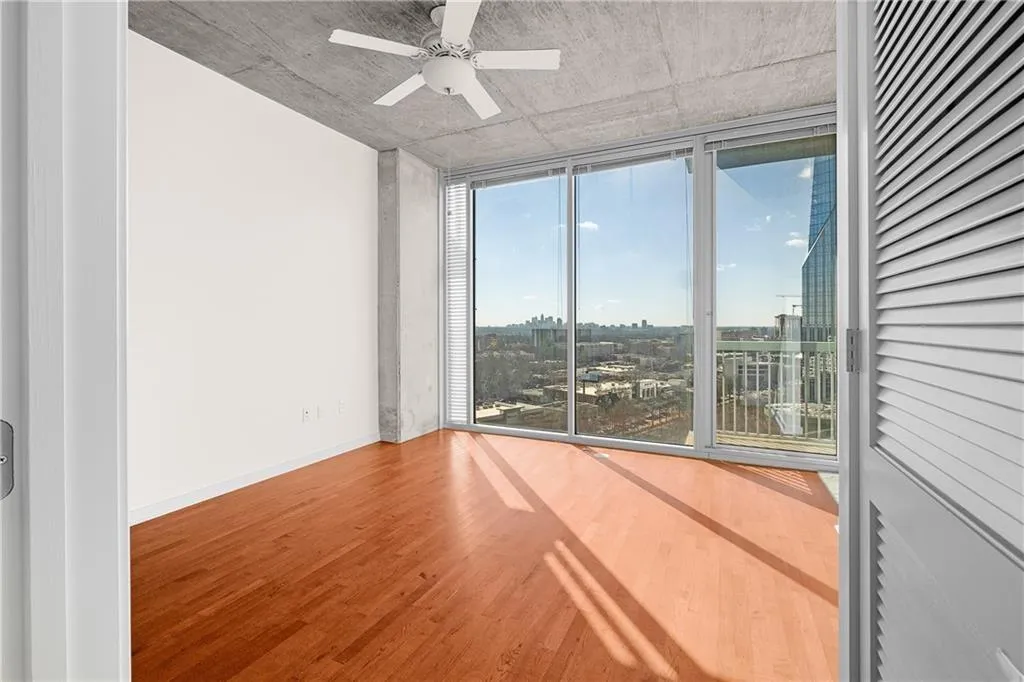 Empty room featuring a view of city, wood finished floors, a wall of windows, baseboards, and ceiling fan