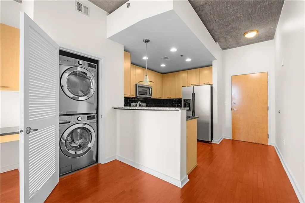 Kitchen with stacked washer / dryer, stainless steel appliances, visible vents, and wood finished floors