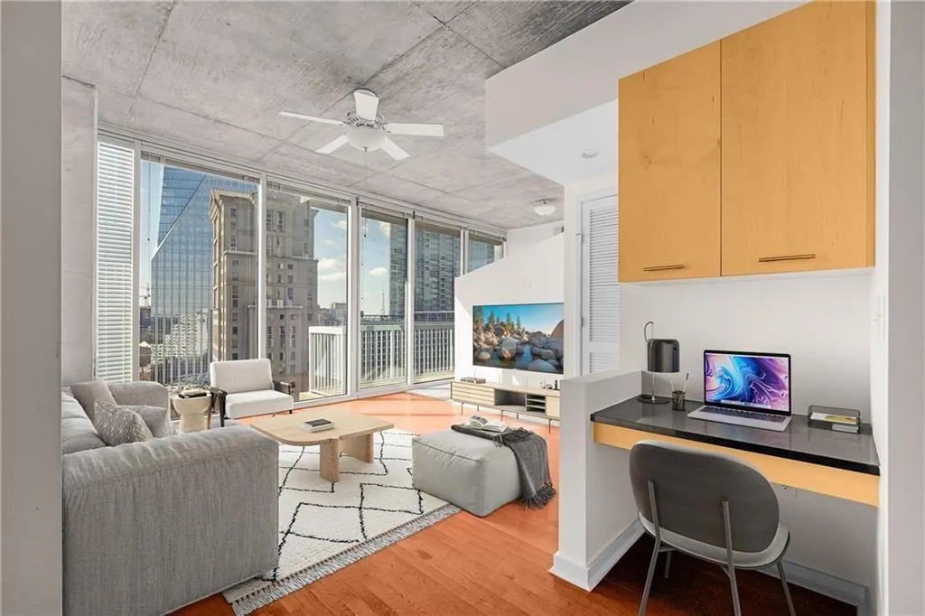 Living area with baseboards, a wall of windows, wood finished floors, built in study area, and a ceiling fan