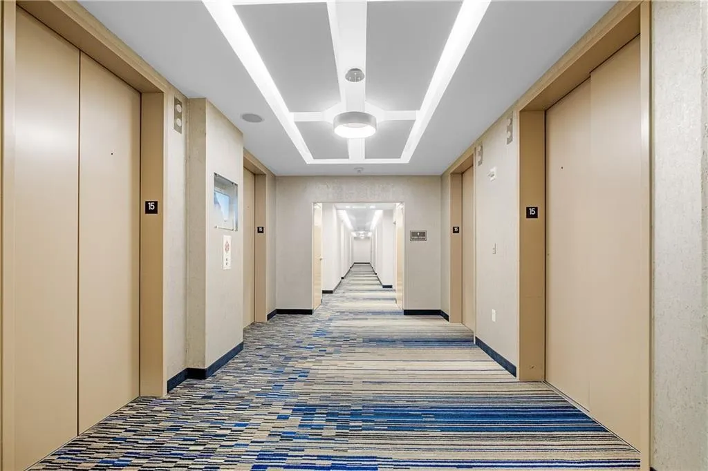 Hallway with a tray ceiling, elevator, and baseboards