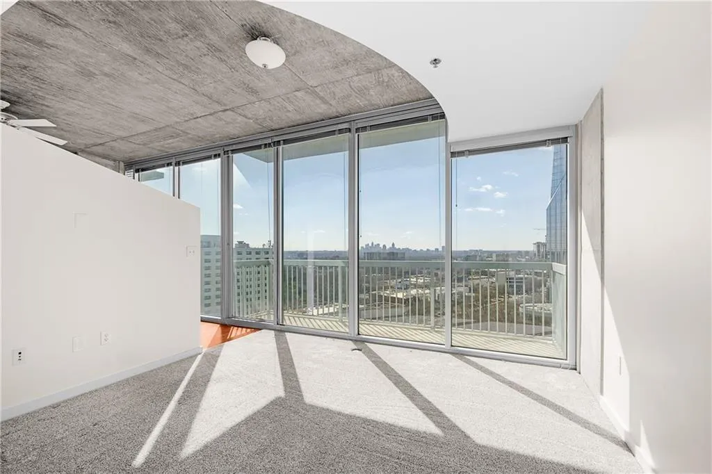 Carpeted empty room featuring a city view, ceiling fan, baseboards, and expansive windows