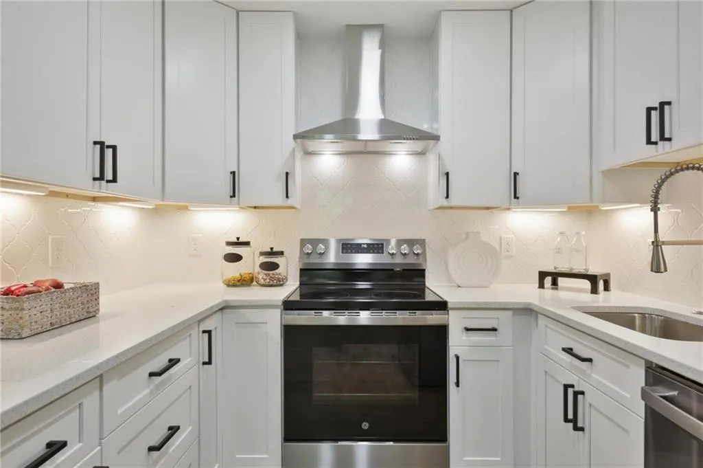 Kitchen with appliances with stainless steel finishes, backsplash, white cabinetry, and wall chimney range hood