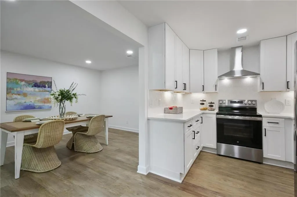 Kitchen featuring stainless steel electric range, light wood-type flooring, decorative backsplash, and wall chimney range hood