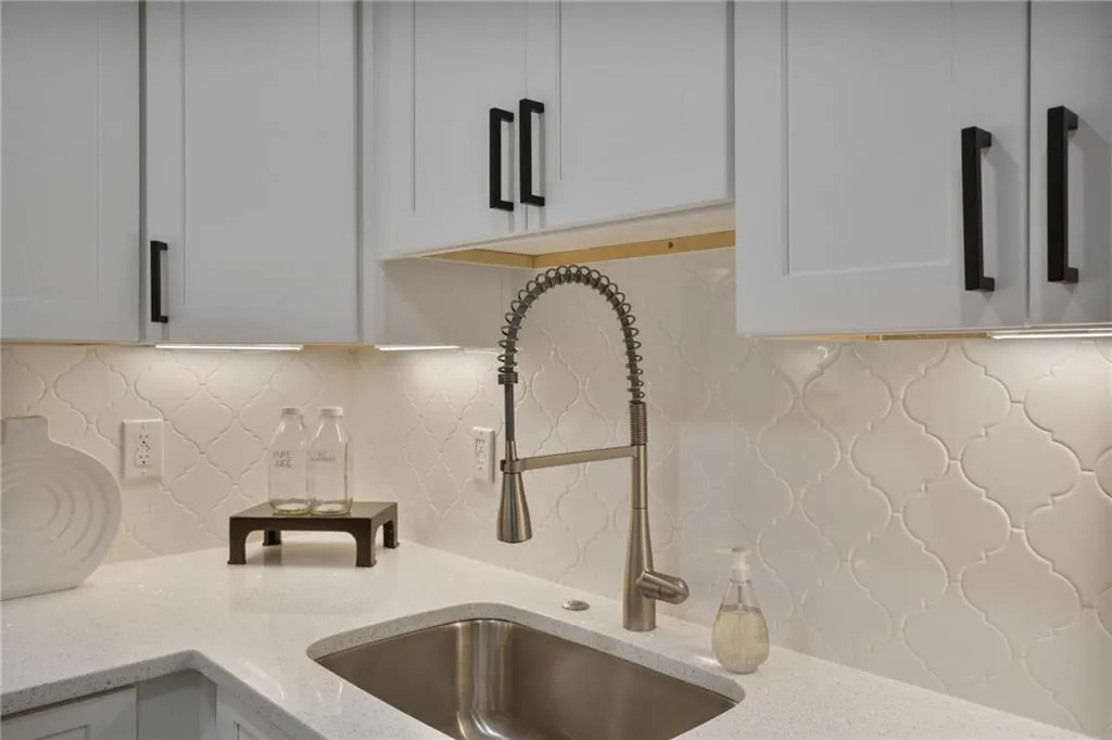 Kitchen featuring sink, light stone counters, tasteful backsplash, and white cabinetry