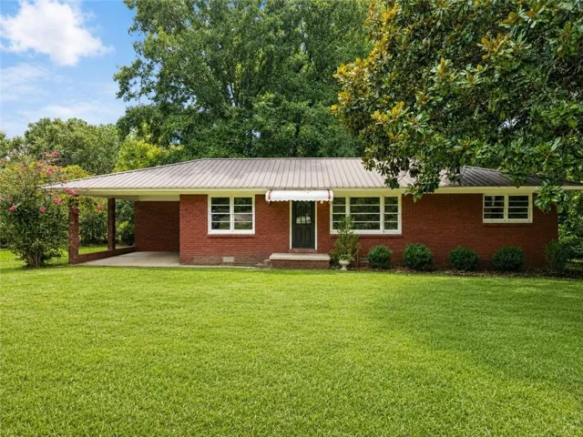 Red brick exterior, metal roof, covered carport, mature landscaping, and a manicured lawn