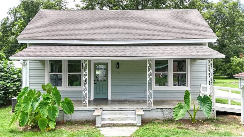 Charming front exterior featuring light blue siding, a covered porch with decorative metal columns, a teal entry door with glass panels, and a gabled roof