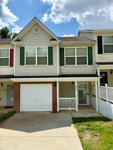 Two-story facade with light-colored siding, green shutters, and an attached single-car garage