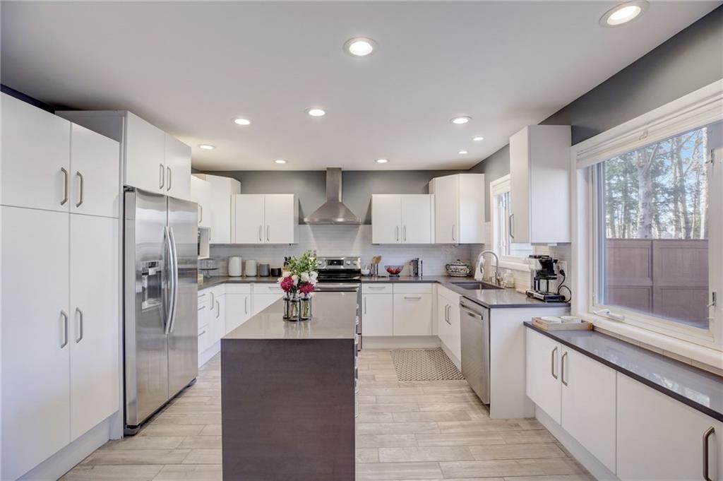 Kitchen with wall chimney exhaust hood, white cabinets, a kitchen island, appliances with stainless steel finishes, and sink