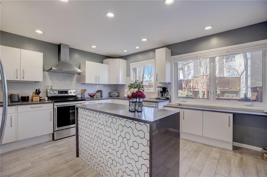 Kitchen featuring a kitchen island, backsplash, white cabinets, appliances with stainless steel finishes, and wall chimney range hood