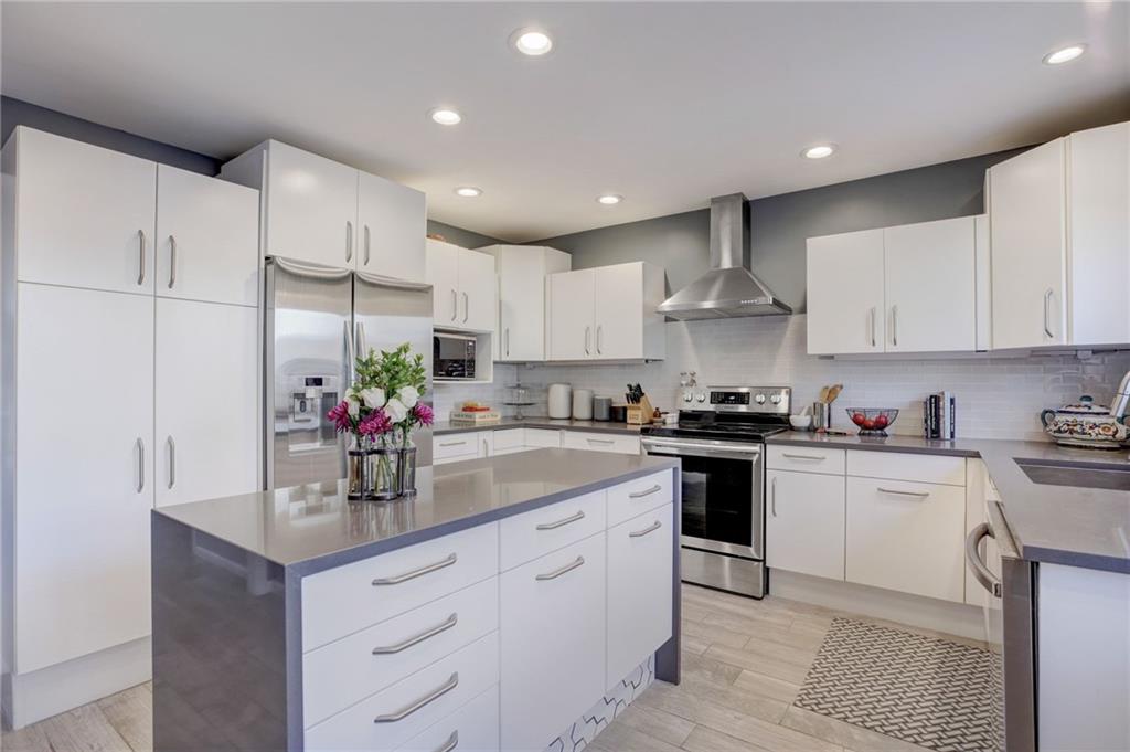 Kitchen with a kitchen island, backsplash, white cabinets, appliances with stainless steel finishes, and wall chimney range hood