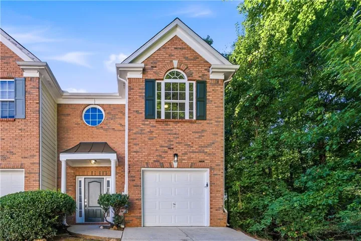 Brick facade townhome featuring a front-facing garage, covered entryway, and mature landscaping