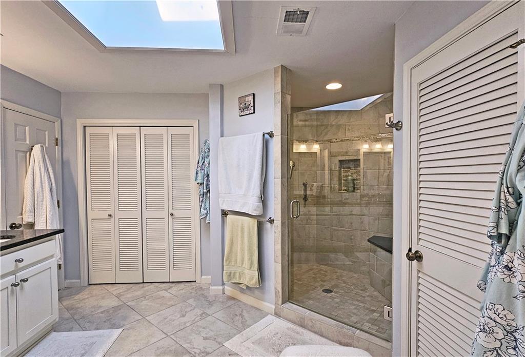 Bathroom featuring a shower with shower door, a skylight, and tile floors