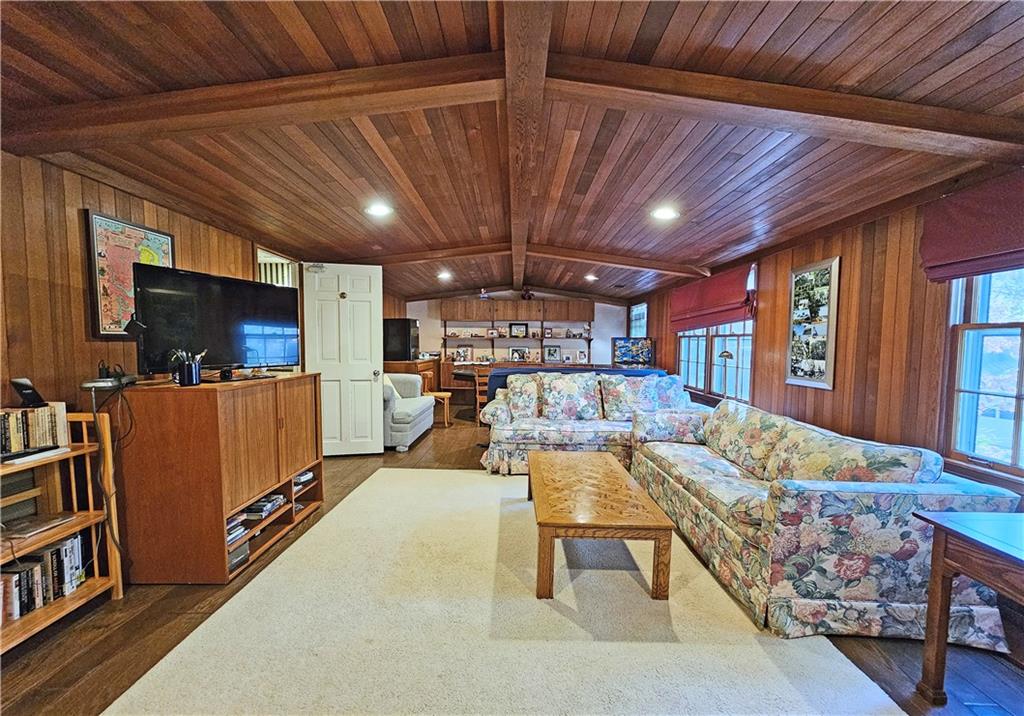Living room with dark hardwood / wood-style flooring, wood walls, wooden ceiling, and lofted ceiling with beams