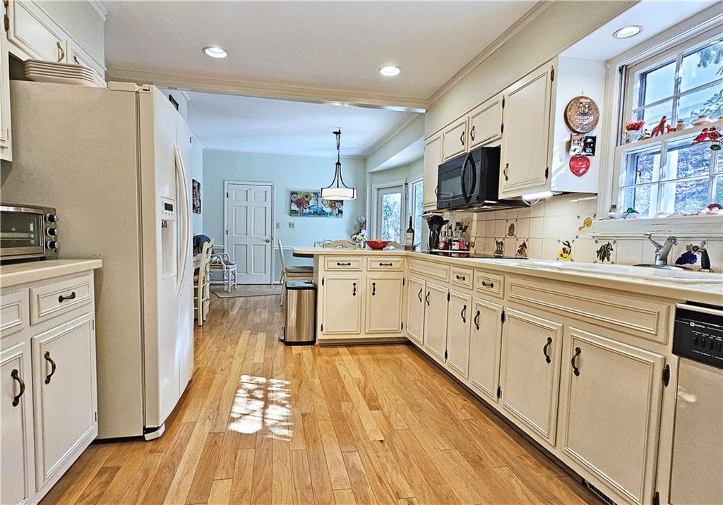 Kitchen with pendant lighting, backsplash, black appliances, and light wood-type flooring