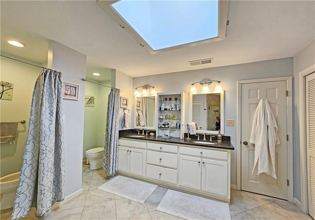Bathroom featuring a skylight, double sink vanity, tile flooring, and toilet