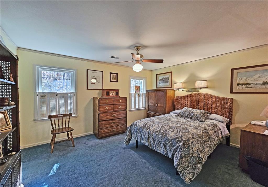Bedroom with multiple windows, dark colored carpet, ceiling fan, and crown molding