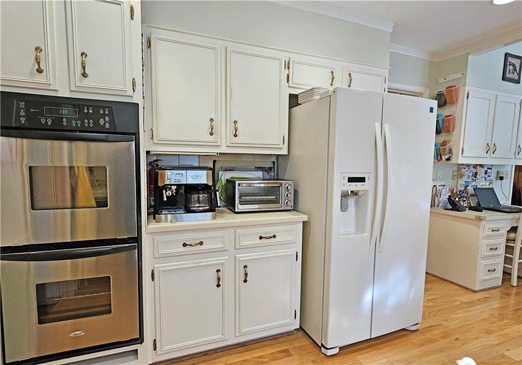 Kitchen with double oven, light hardwood / wood-style floors, white fridge with ice dispenser, and white cabinetry