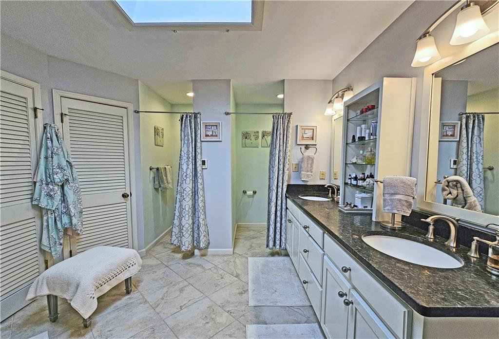 Bathroom featuring large vanity, dual sinks, tile floors, and a skylight