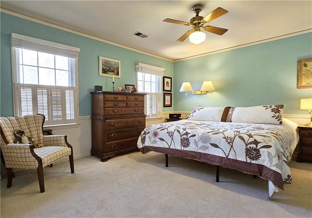 Carpeted bedroom with ceiling fan and ornamental molding