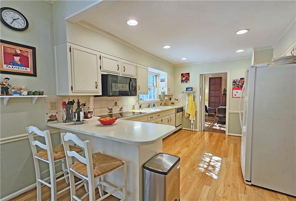 Kitchen featuring light hardwood / wood-style floors, black appliances, a kitchen breakfast bar, and tasteful backsplash