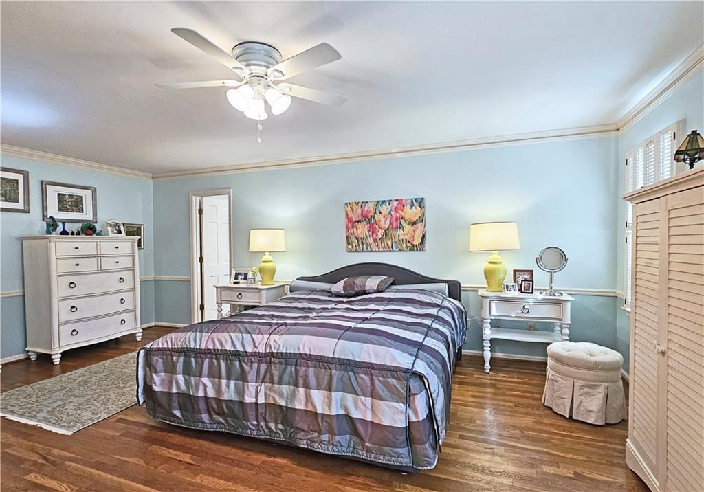 Bedroom with ceiling fan, dark wood-type flooring, and ornamental molding