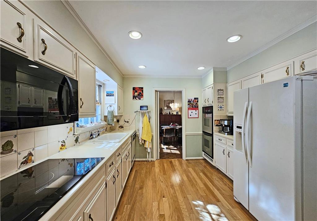 Kitchen with light hardwood / wood-style flooring, white refrigerator with ice dispenser, backsplash, white cabinets, and sink