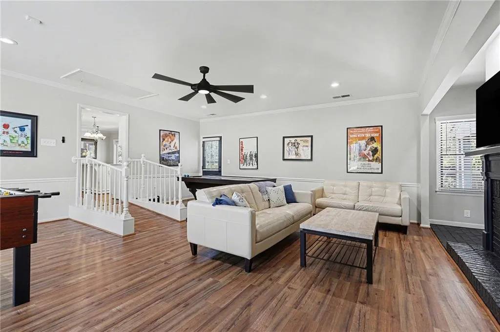 Living area featuring ceiling fan, a fireplace with raised hearth, recessed lighting, dark wood-style flooring, and crown molding