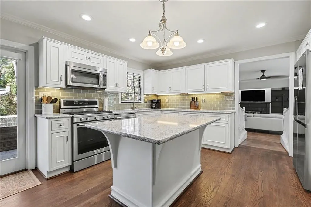 Kitchen with stainless steel appliances, light stone counters, white cabinetry, dark wood-type flooring, and ornamental molding