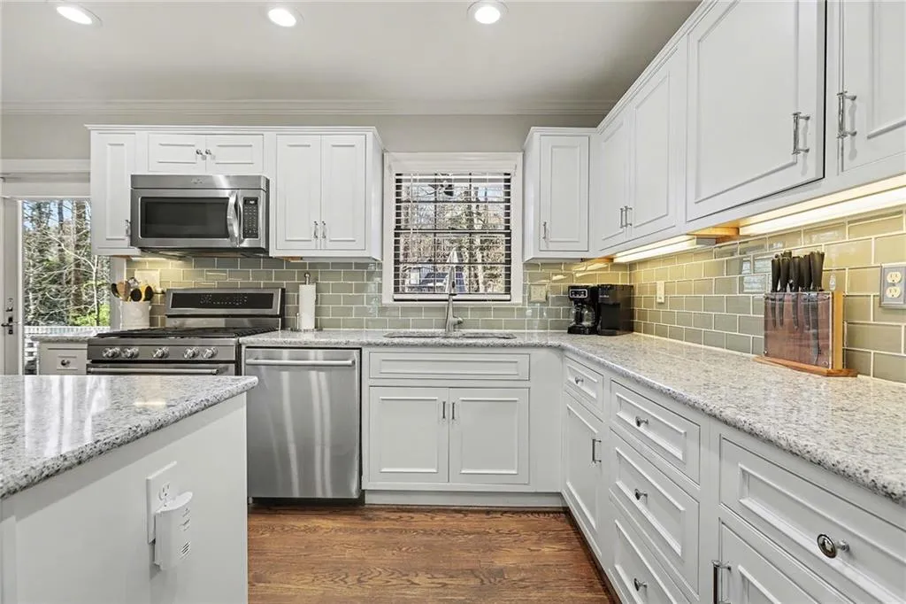 Kitchen with white cabinets, stainless steel appliances, ornamental molding, light stone countertops, and dark wood-style floors