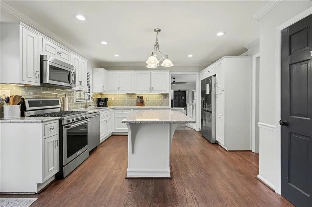 Kitchen with stainless steel appliances, light stone counters, white cabinetry, backsplash, and crown molding