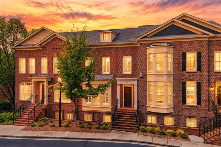 Brick facade townhome featuring multiple bay windows, black shutters, and gabled rooflines