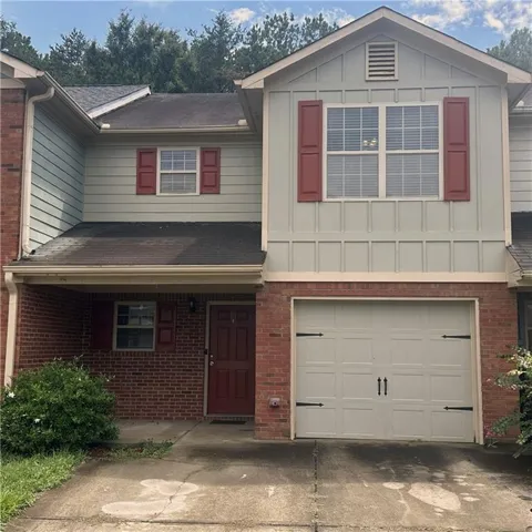 Brick facade with lightsiding, covered entry, attached garage with decorative hardware, and red window shutters