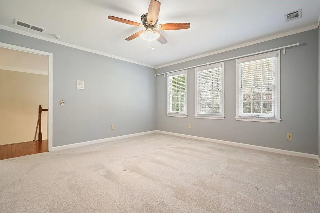 Empty room featuring visible vents, crown molding, ceiling fan, and carpet