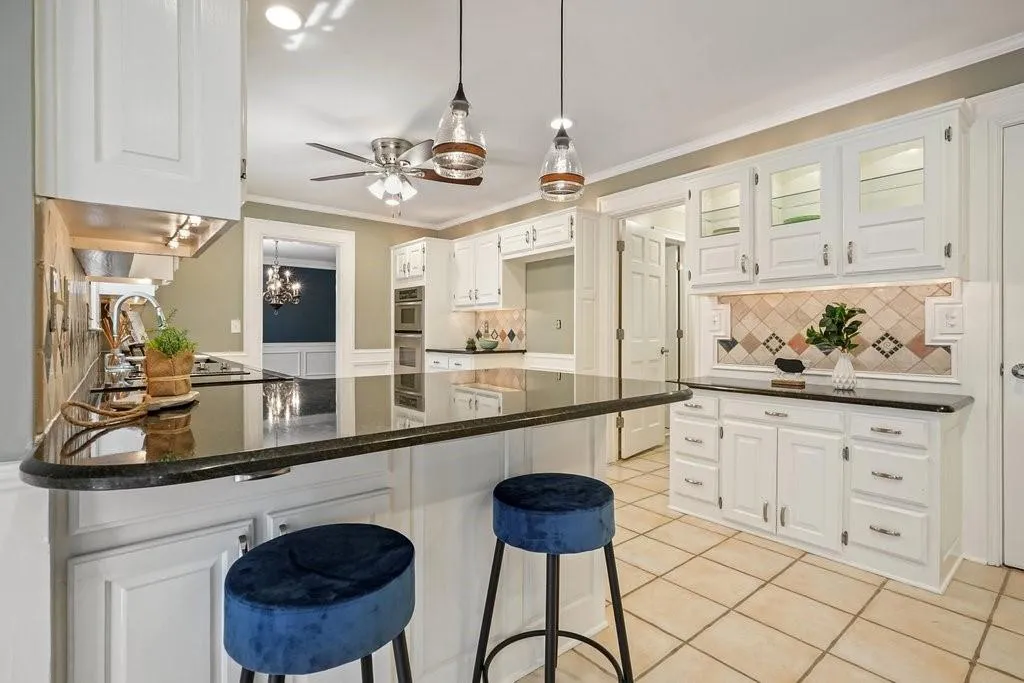 Kitchen with light tile patterned flooring, crown molding, a peninsula, ceiling fan with notable chandelier, and white cabinets
