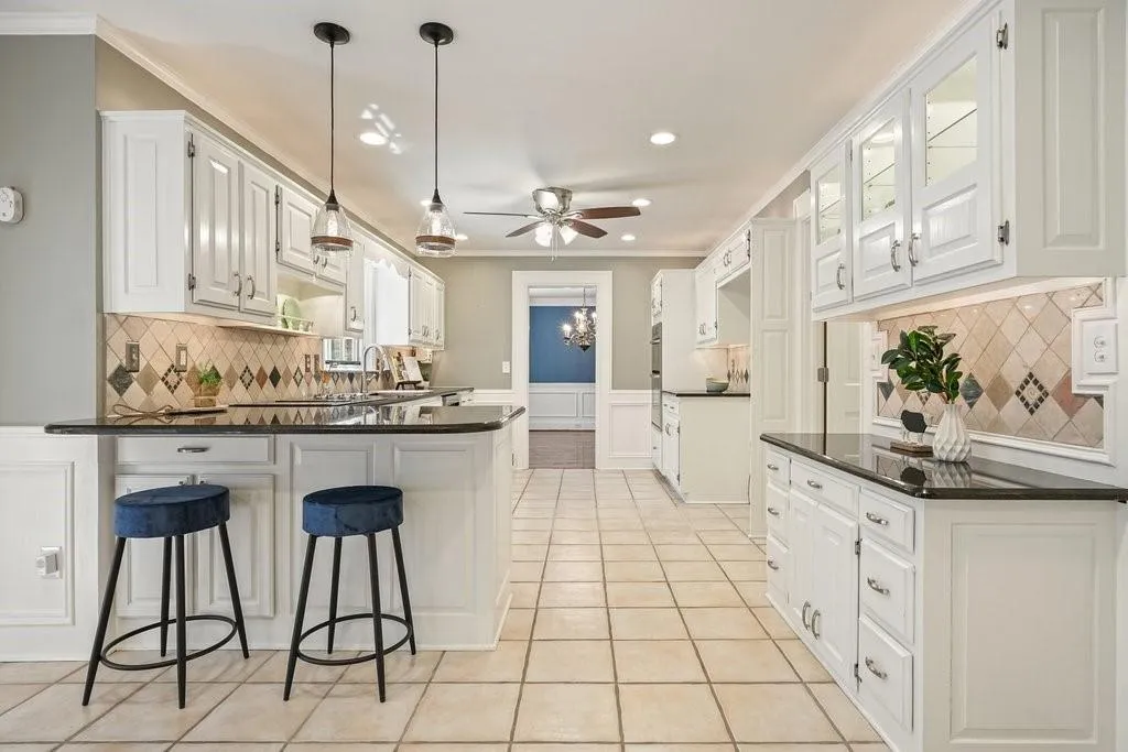 Kitchen with light tile patterned flooring, crown molding, a ceiling fan, a peninsula, and dark countertops