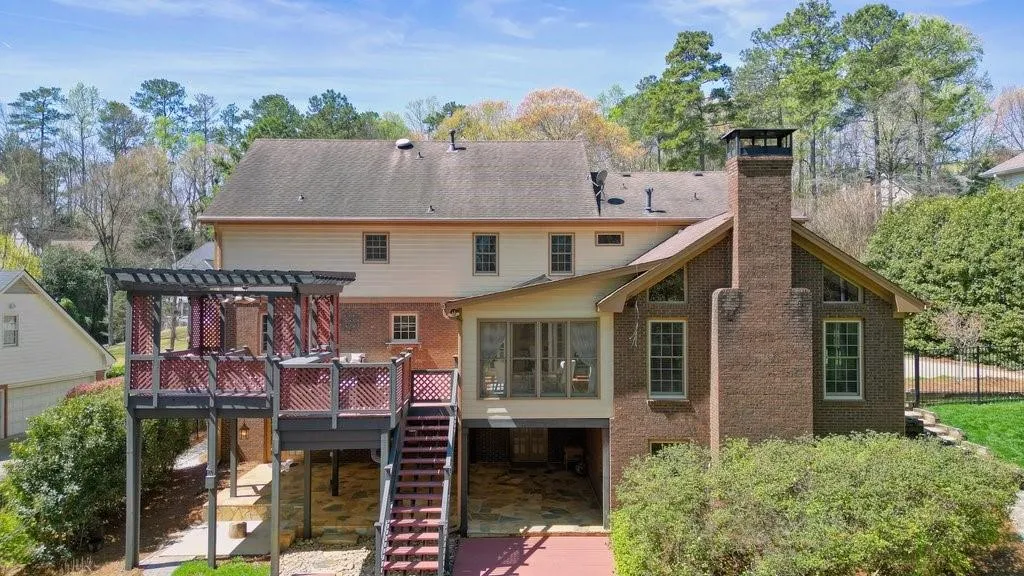 Back of house featuring a wooden deck, stairs, a chimney, brick siding, and a pergola