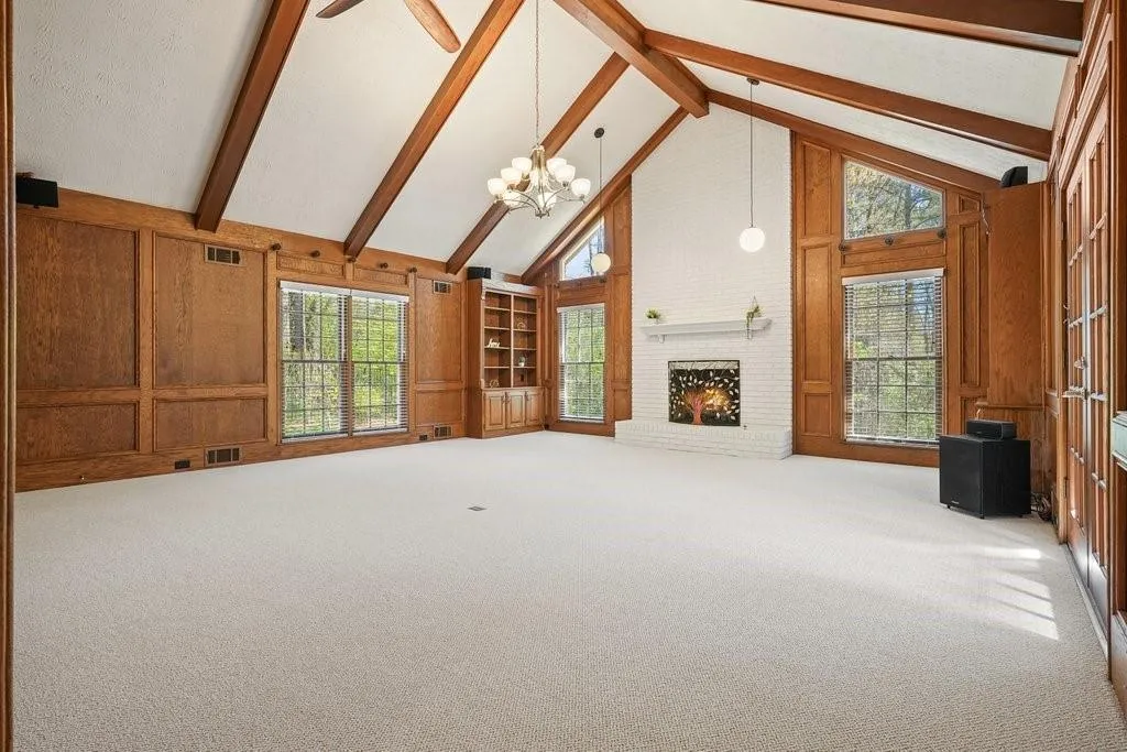 Unfurnished living room with beam ceiling, wooden walls, a fireplace, and visible vents