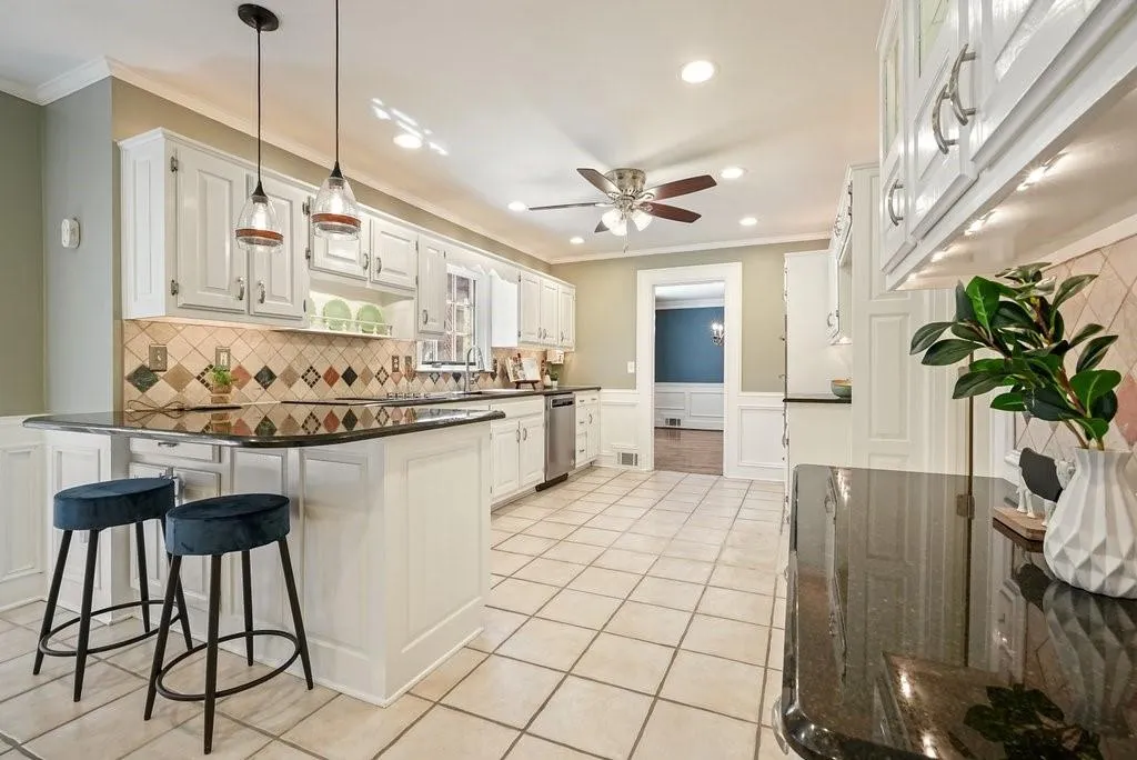 Kitchen featuring crown molding, light tile patterned floors, stainless steel dishwasher, a peninsula, and wainscoting