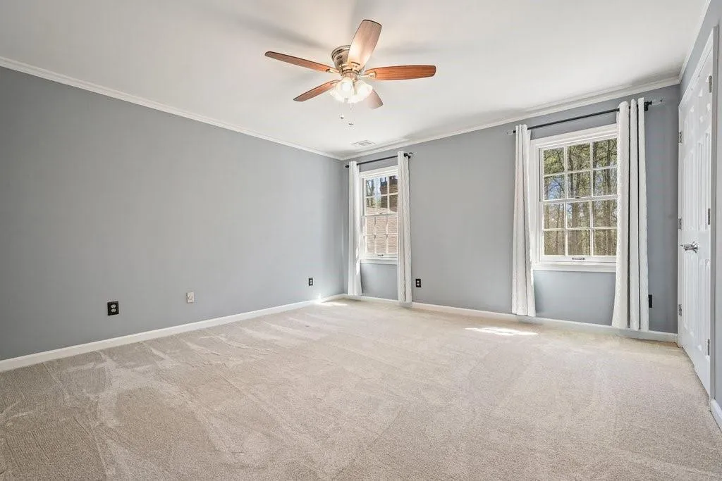 Empty room featuring a ceiling fan, ornamental molding, baseboards, and light colored carpet