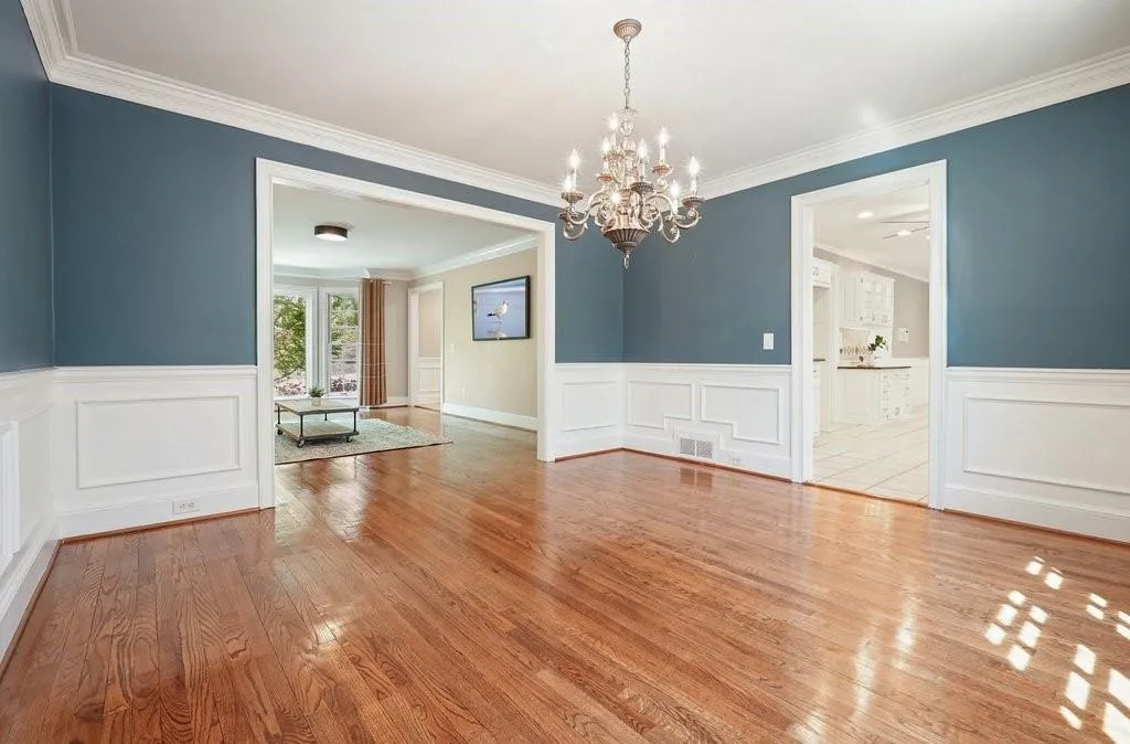 Empty room featuring a wainscoted wall, visible vents, wood finished floors, and a chandelier