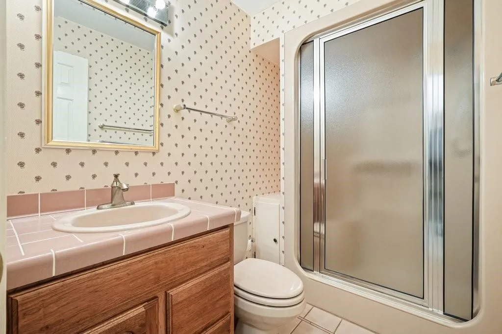 Full bath with toilet, vanity, a shower stall, tile patterned flooring, and wallpapered walls