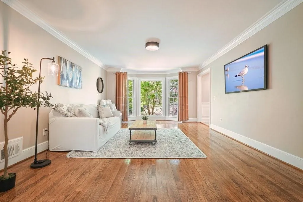 Living room with baseboards, visible vents, wood finished floors, and ornamental molding