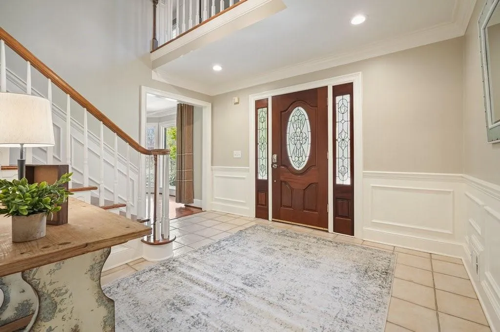 Foyer with tile patterned floors, crown molding, a decorative wall, and stairway