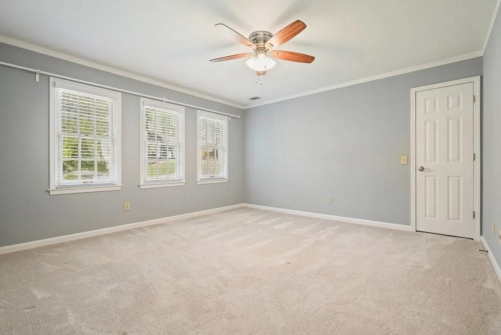 Empty room featuring crown molding, baseboards, visible vents, a ceiling fan, and light carpet