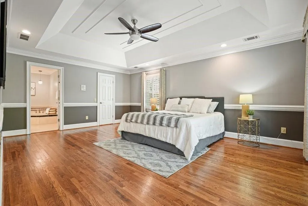 Bedroom featuring a tray ceiling, ornamental molding, baseboards, visible vents, and wood finished floors
