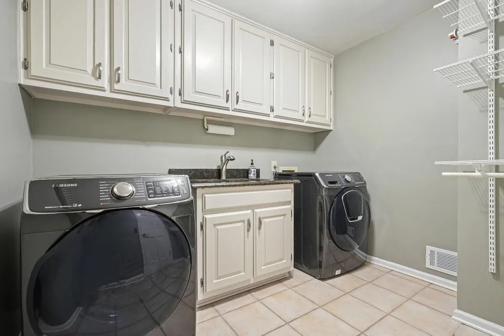 Clothes washing area with visible vents, hookup for a washing machine, a sink, cabinet space, and light tile patterned floors