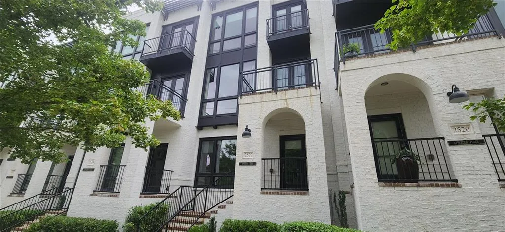 Modern townhome facade featuring white painted brick, black framed windows, and multiple private balconies