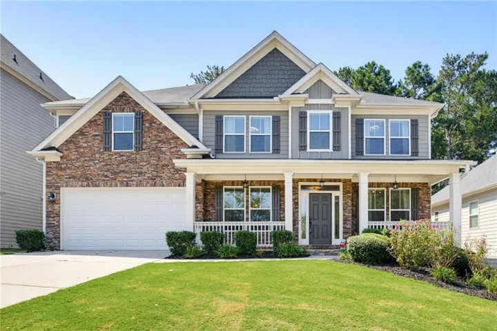 Two-story exterior with stone and siding accents, prominent front porch with white columns, two-car garage, and a landscaped front yard